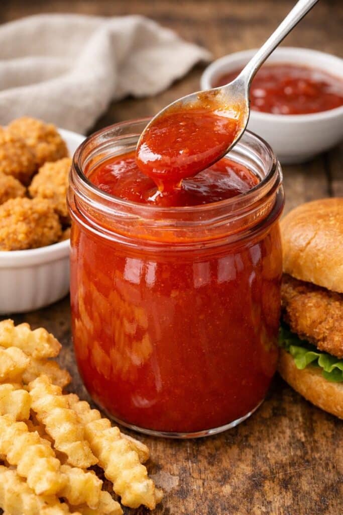 Chick-fil-A Polynesian sauce copycat in a glass jar with a spoon, served with nuggets and fries on a rustic wooden surface.