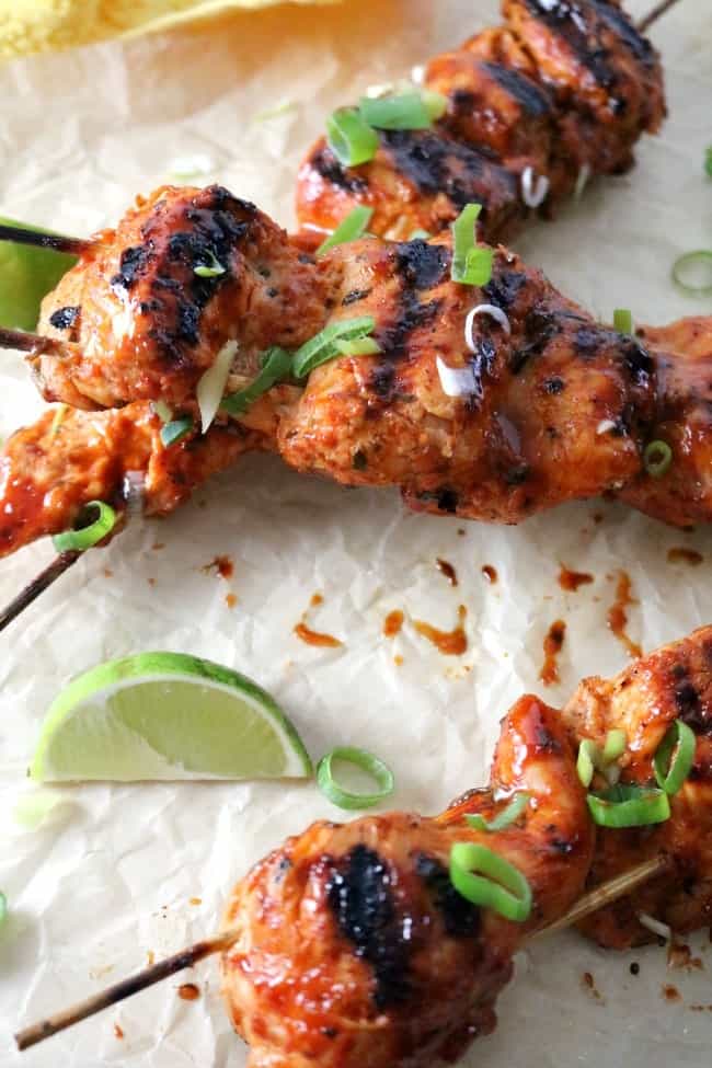 Korean chicken skewers in a brown paper background with a wedge of lime and sliced green onions