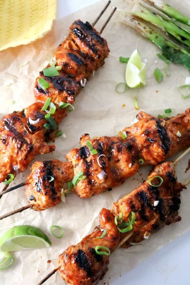Korean chicken skewers on a brown paper with lime wedges and grilled green onions.