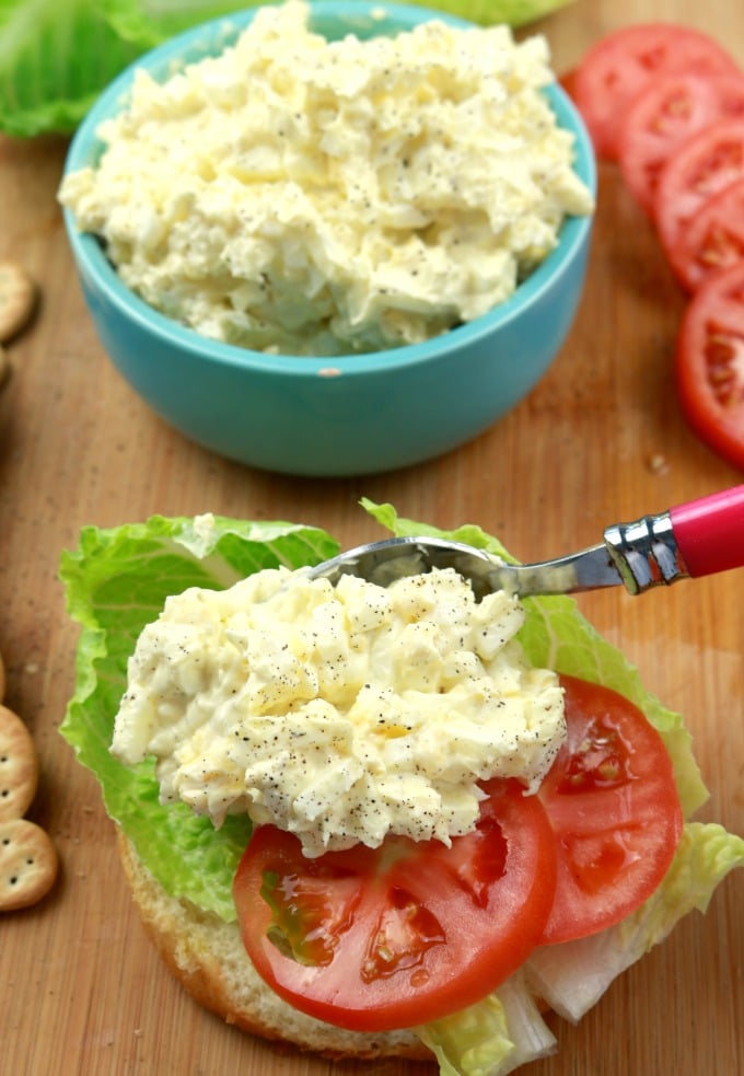 an inage of egg salad being spread on a sandwich with lettuce and tomatoes.