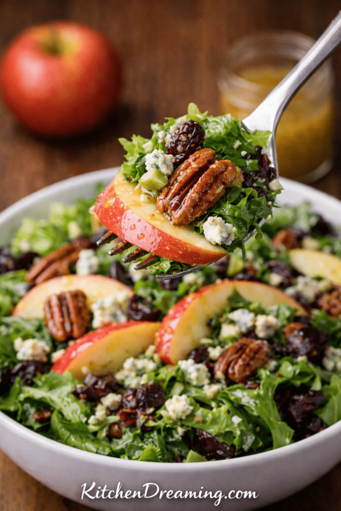 Forkful bite shot of apple vinaigrette salad with apple slices, pecans, dried fruit, and blue cheese coated in apple vinaigrette dressing.