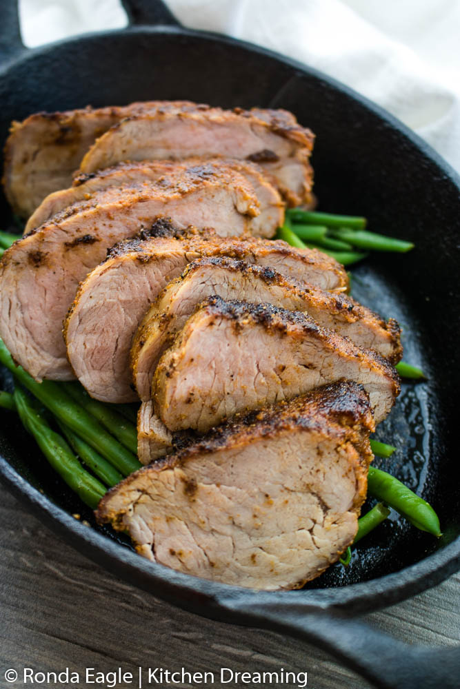An oblong cast iron skillet filled with roasted green beans and sliced pork tenderloin.