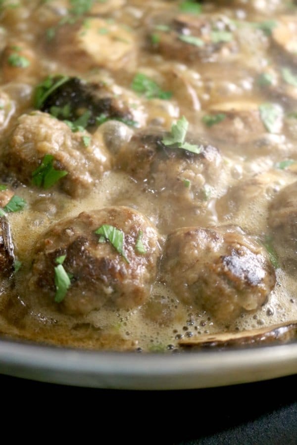 An image of salisbury steak meatballs cooking in a pan of brown mushroom gravy