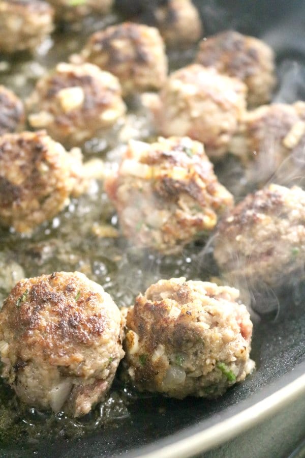 A close up image of salisbury steak meatballs browning in a Teflon skillet