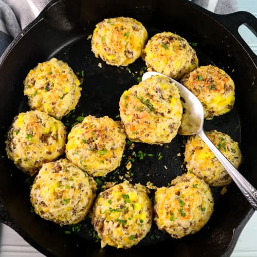 A pan of baked sausage cheese biscuits. Two biscuits have been removed; a silver serving spatula sticks out of the right side of the pan.