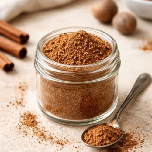 Homemade Pumpkin Pie Spice Blend in a glass jar with a spoon on a neutral countertop.