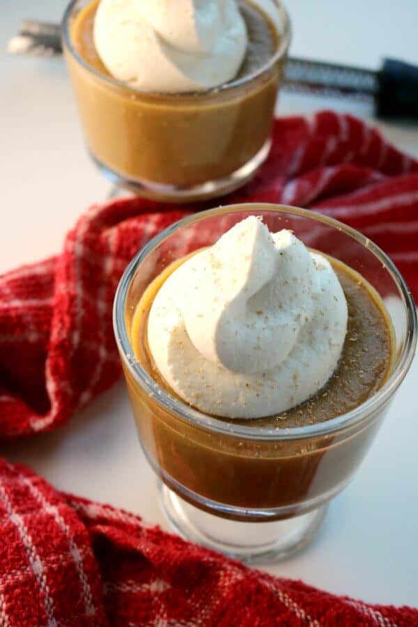 Two cups of pumpkin pie pudding topped with fresh whipped cream and a light shaving of fresh nutmeg.