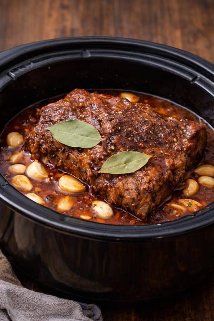 Slow. Cooker Portuguese Pot Roast cooking in a crock pot with garlic and bay leaves.