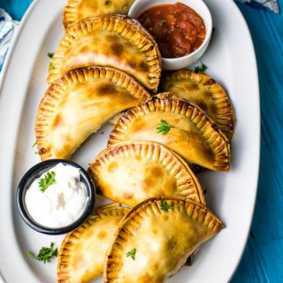 A plate of baked beef empanadas with sour cream and salsa for dipping.