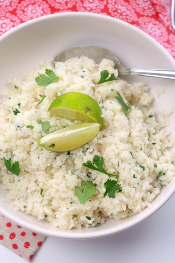 An overhead shot of a bowl of 5-minute Cilantro lime rice garnished with 2 lime wedges and extra torn cilantro. 