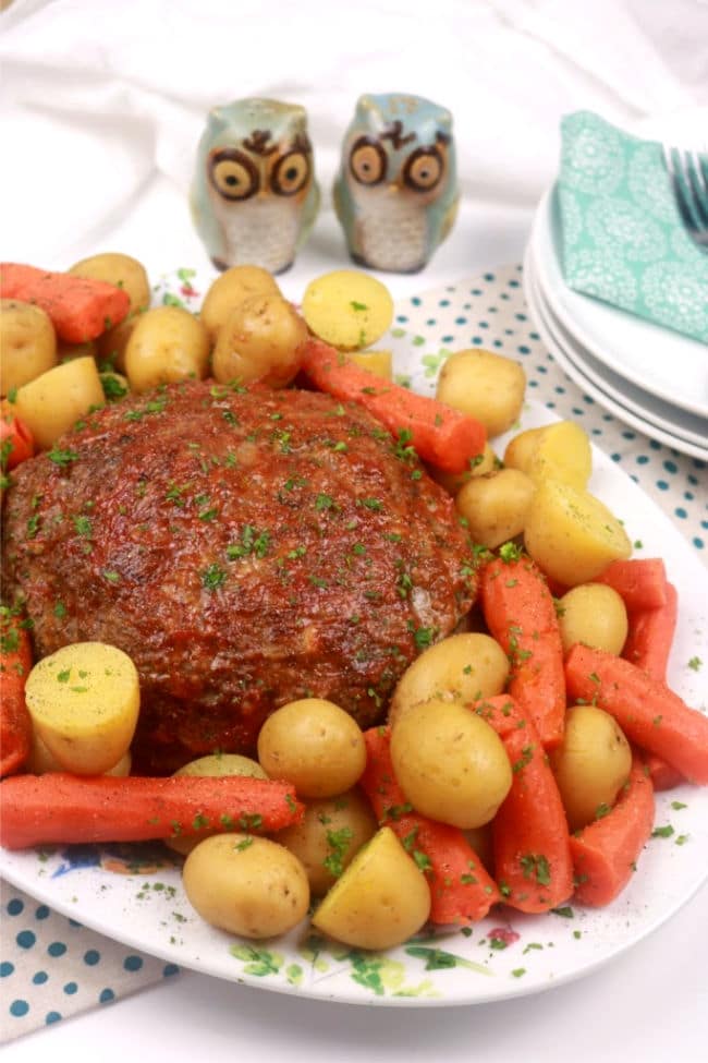 A platter of instant Pot Pressure Cooker Meatloaf dinner on a white table with dishes and blue polka dotted napkins.