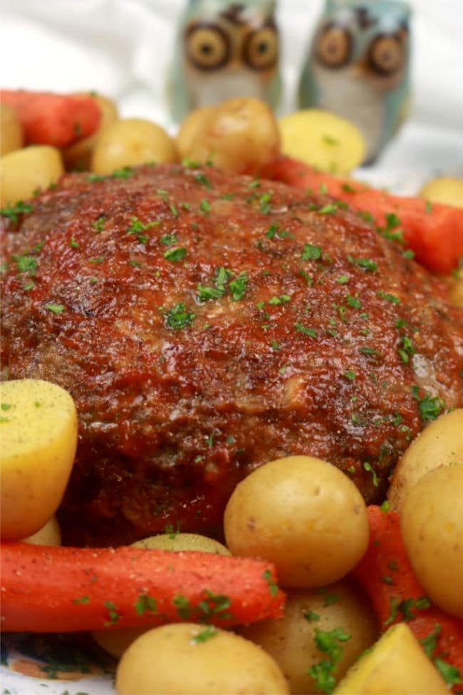 An up close photo of instant pot meatloaf on a platter with steamed potatoes and carrots.