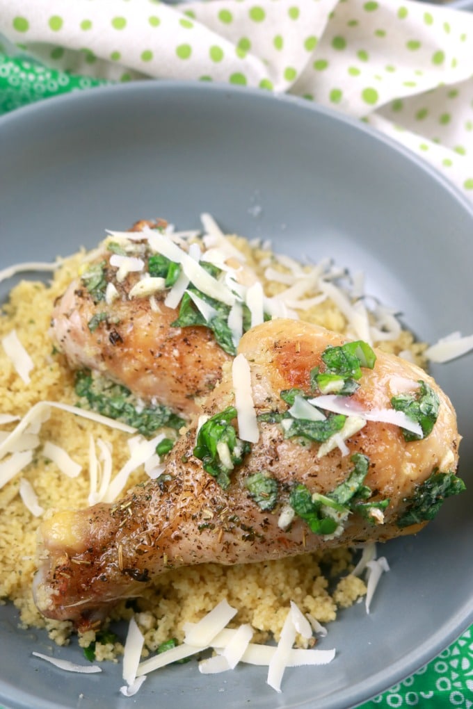 A close-up photo of Garlic Parmesan chicken plated over couscous, drizzled with garlic basil oil and a sprinkle of parmesan cheese. 