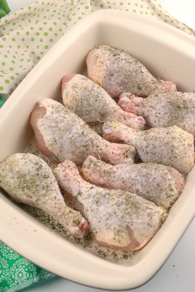 A baking pan filled with chicken legs that have been sprinkled with an Italian herb mixture.