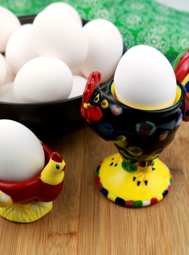 A bowl of whole raw eggs in their shells and two egg holder cups aslo holding eggs