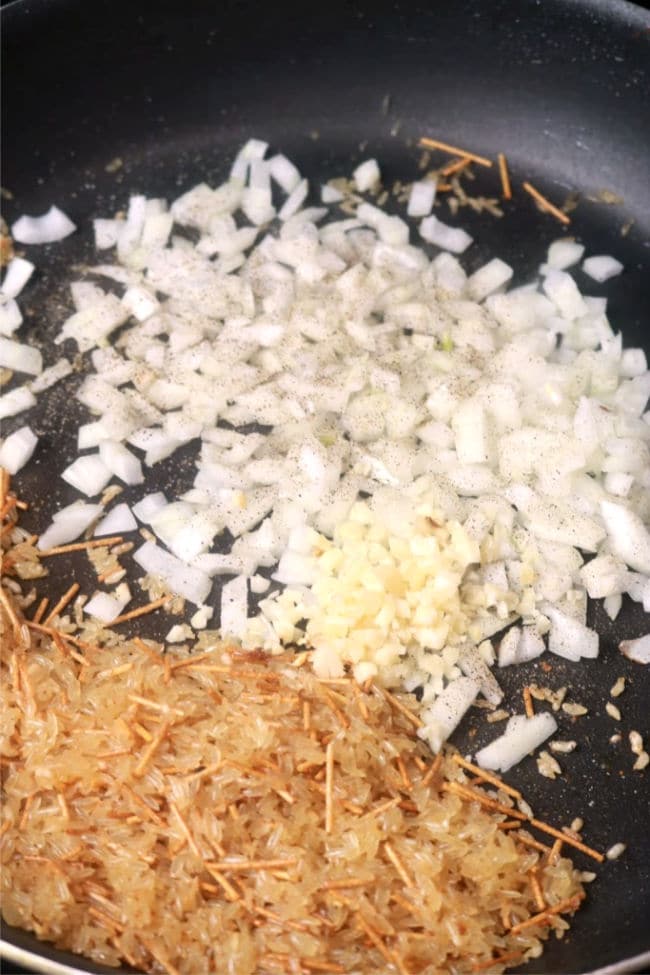 Onions and garlic being sauted in the skillet wit the rice and broken spaghetti.
