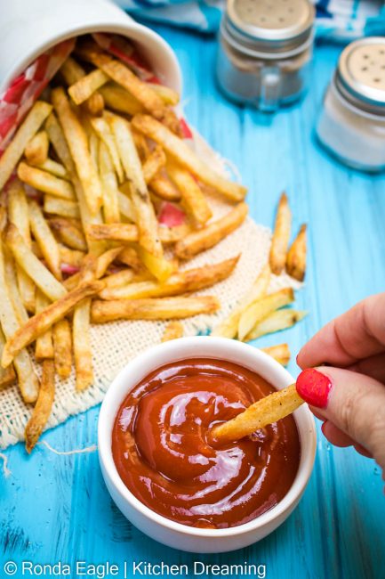 An image of  French fries being dipped into a small bowl of ketchup/