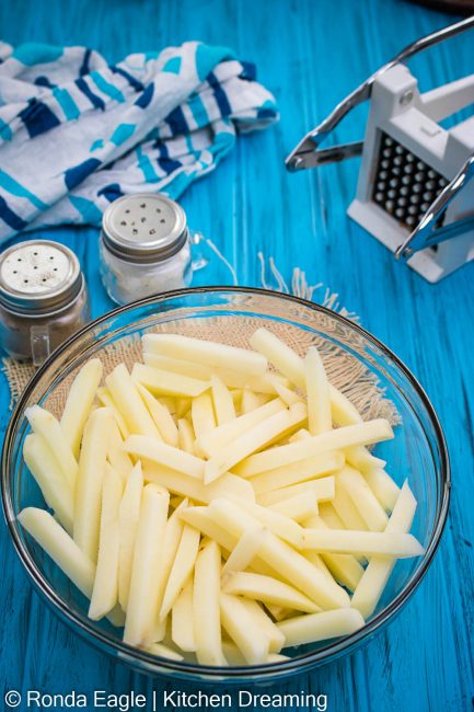 An image of a glass bowl filled with raw potato sticks which have been soaked and dried for frying.