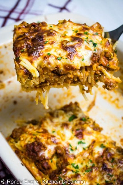 In image of a baked spaghetti casserole in a baking pan with a slice up on a spatula.