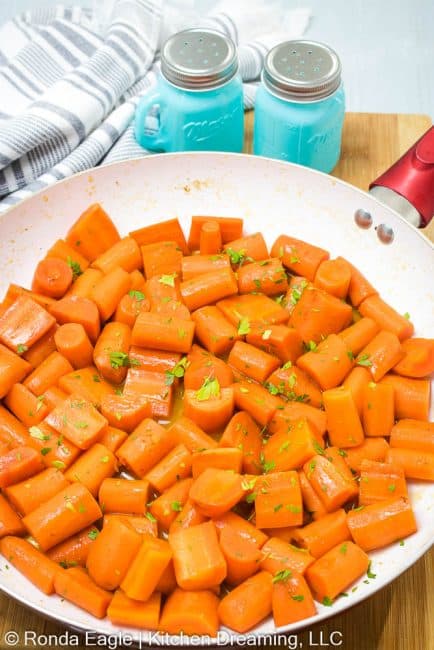 A skillet filled with glazed carrots garnished with freshly chopped parsley.