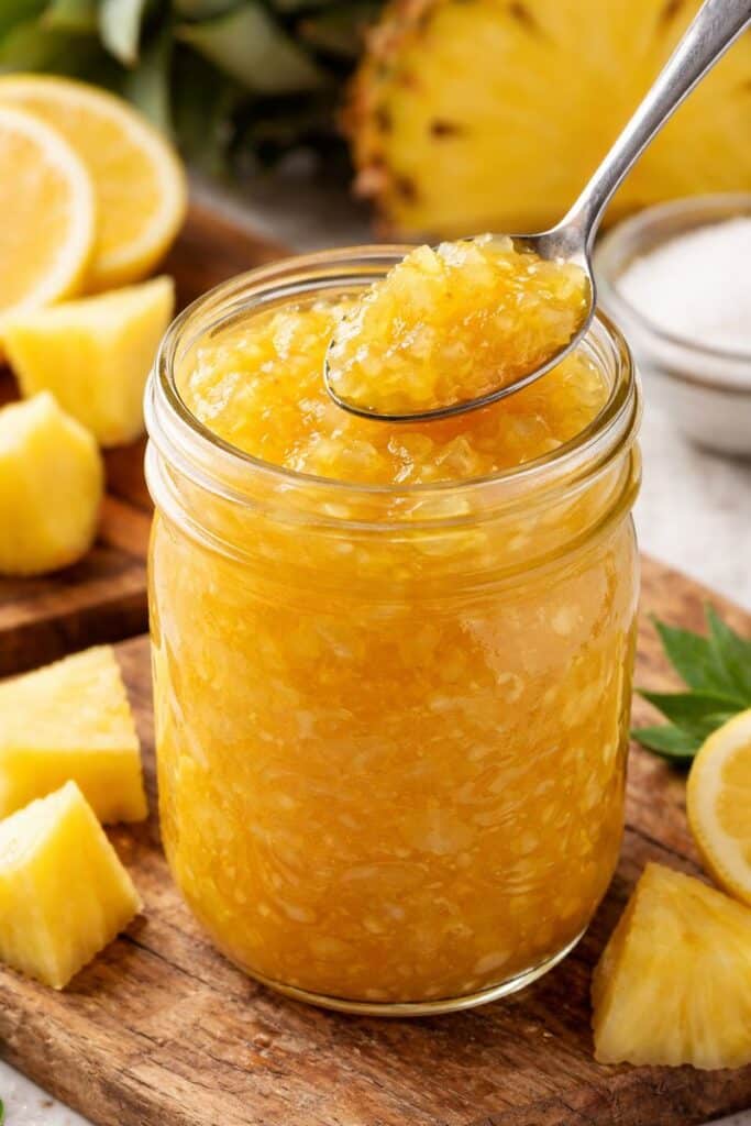 Small batch pineapple jam in a mason jar with a spoon, no pectin, glossy golden texture, fresh pineapple and lemon in the background.