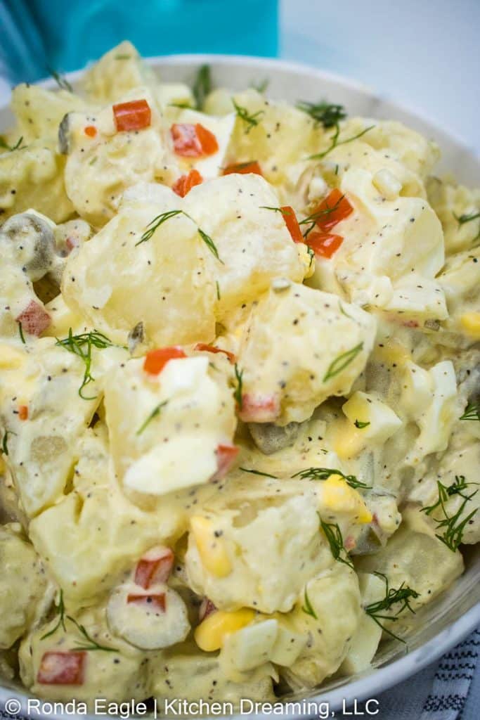 a close-up image of a bowl of potato salad with olives. It is garnished with some fresh dill. 