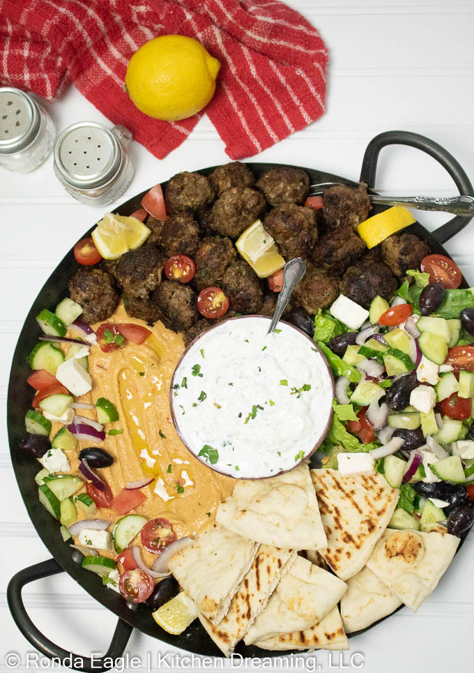 Greek charcuterie platter containing Greek meatballs, hummus, pita triangles, greek cucumber & feta salad, and tzatziki sauce.