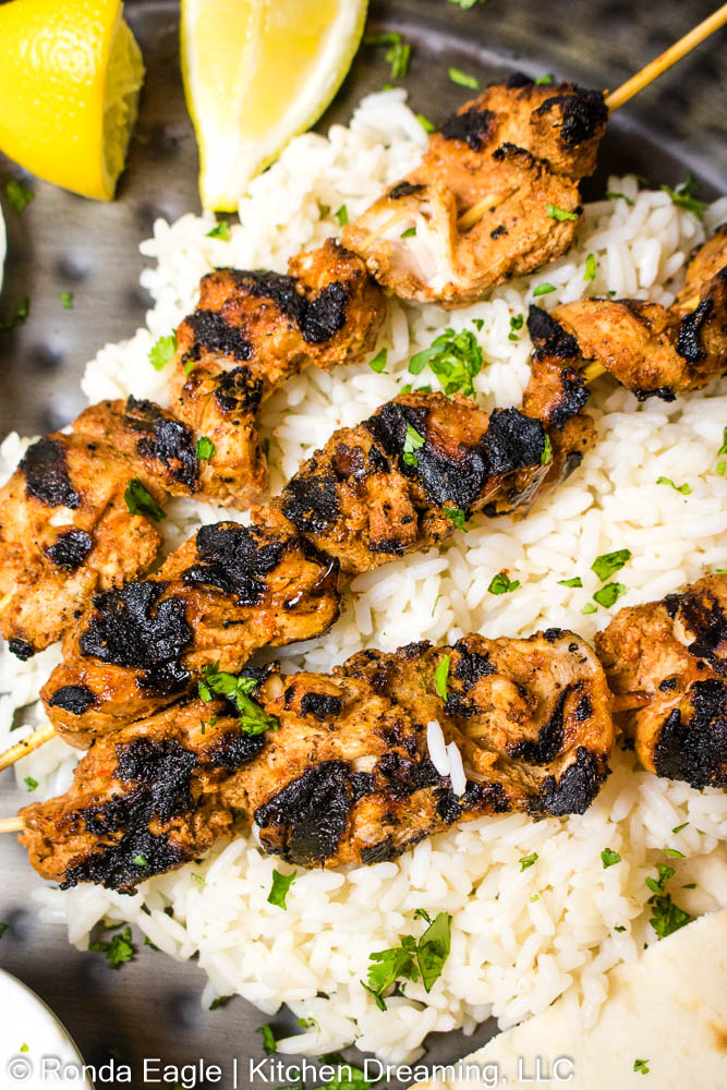Three Grilled Tandoori Chicken skewers on a bed of rice.