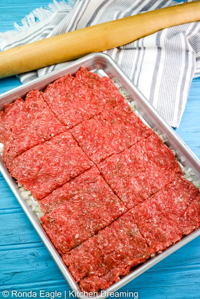 A sheet pan of onions and a layer of ground beef rolled thin to form the patties of the Krystal burger.