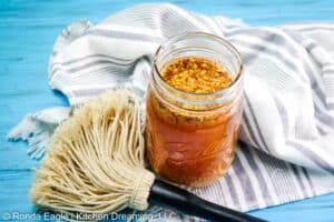 A jar of Carolina Mopping Sauce surrounded by a grey striped towel and a BBQ mop.