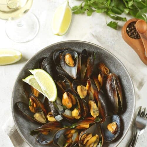 A pin image of a bowl of mussels in white wine sauce on a table.