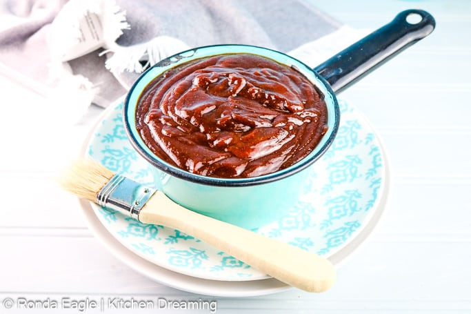  A small blue vintage enamel sauce pan holds the sweet & Tangy BBQ sauce. A basting brush rests across the dish under the pan.