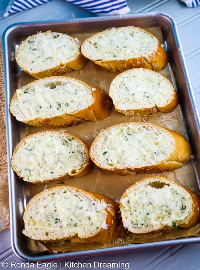 A tray of sliced baguette that has been topped with compound butter and cheese.