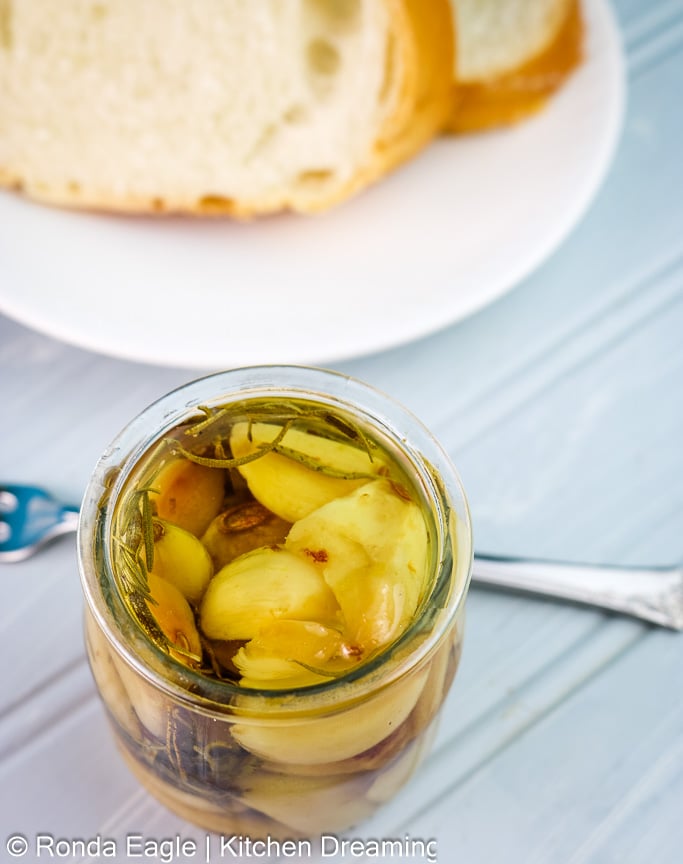 A small jar of garlic confit on a table with slices of crusty bread.