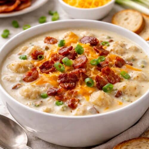 Creamy loaded baked potato soup in a white bowl topped with melted cheddar, crispy bacon, and green onions.