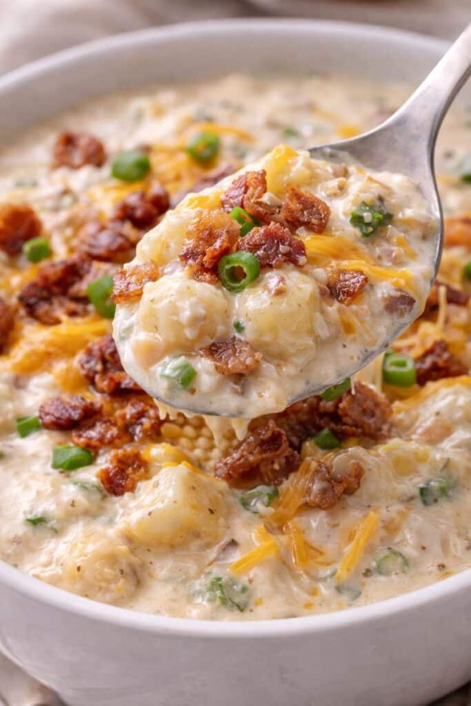 Spoonful of creamy loaded baked potato soup with potato chunks, melted cheddar cheese, bacon bits, and green onions over a creamy base.