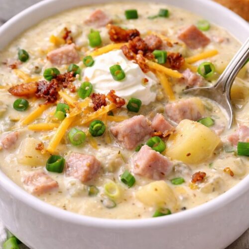 Creamy leftover ham chowder topped with cheddar, bacon, and green onions in a white bowl.