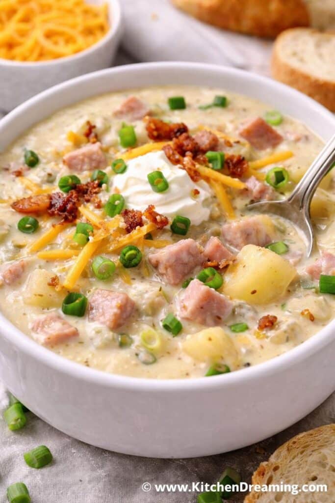 Creamy leftover ham chowder topped with cheddar, bacon, and green onions in a white bowl.