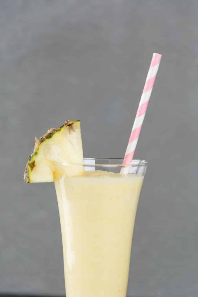 A glass filled with Dole whip smoothie and a slice of fresh pineapple garnish.