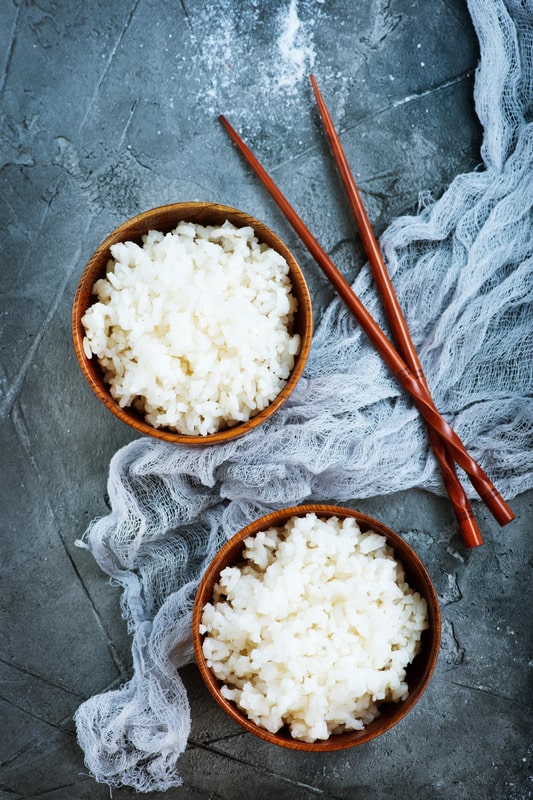 two bowls of white rice on a grey background with grey cheesecloth.