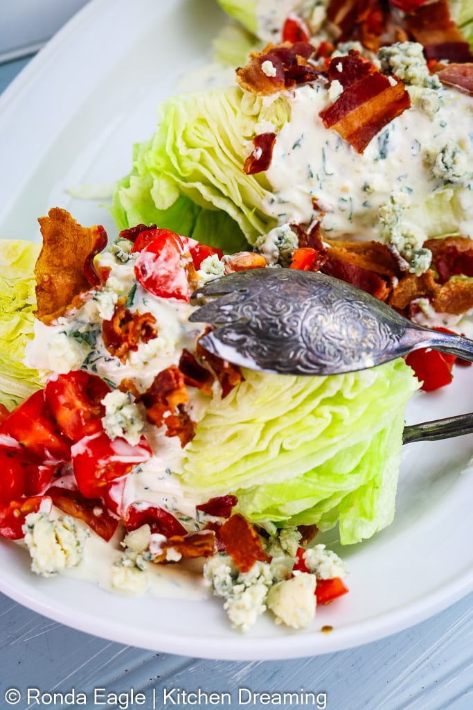 an up close photo of an Iceberg wedge salad topped with creamy herbed ranch dressing, bacon, and cherry tomatoes. 