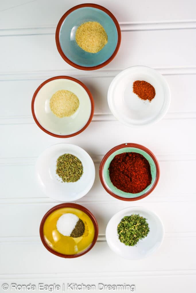Seven small bowls of various pantry ingredients used to make a Blackening seasoning recipe. 