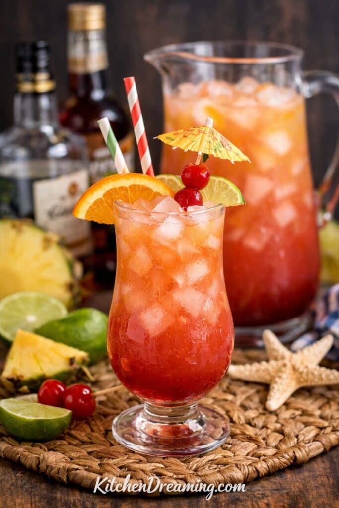 Caribbean Rum Punch Recipe served over ice in a hurricane glass with orange, lime, and cherries.