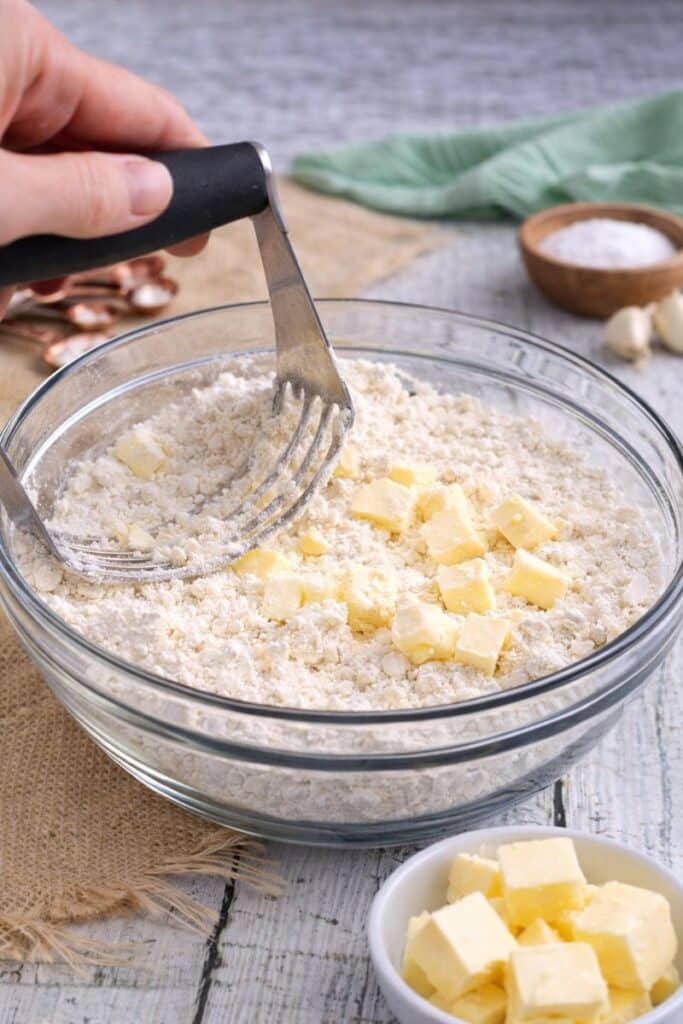 Homemade Baking Mix (Easy Bisquick Substitute with 5 Pantry Ingredients) 3 Glass bowl filled with homemade Bisquick baking mix on a rustic kitchen surface, with butter and pantry ingredients in the background.