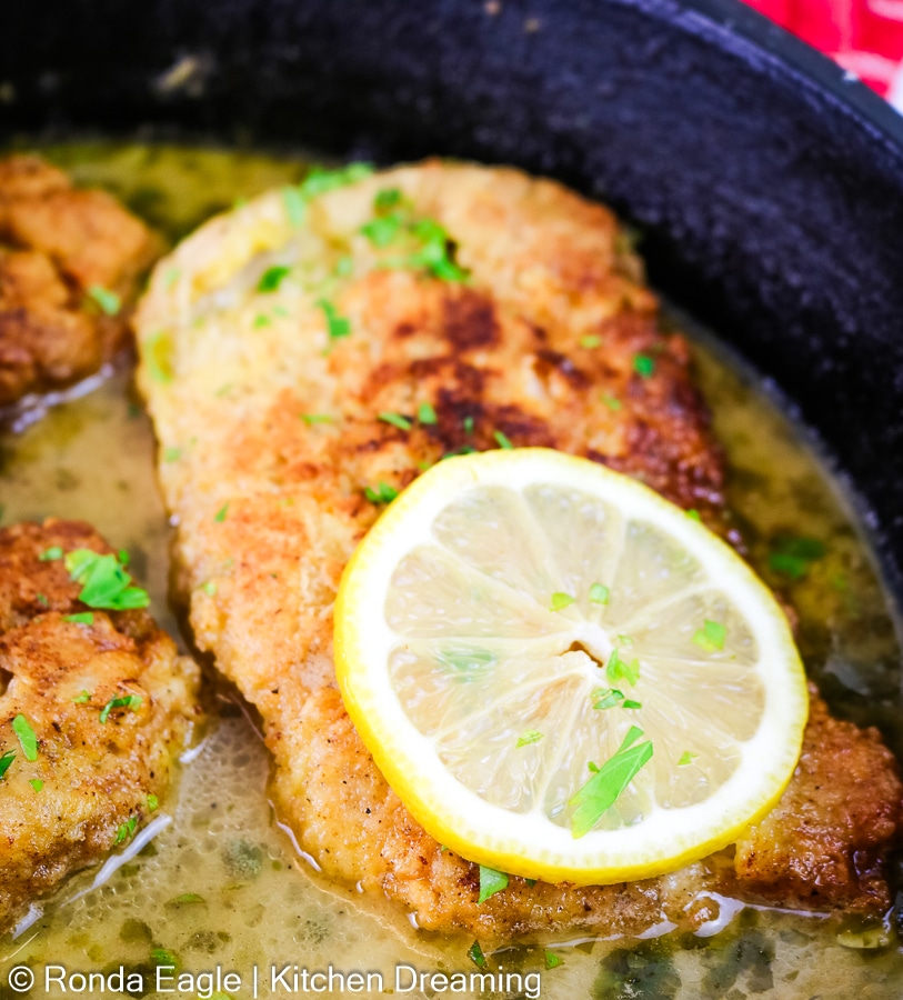 A close up of a chicken cutlet smothered in lemon butter caper sauce. 