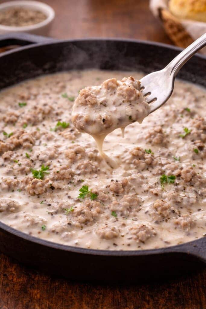 how to make sausage gravy from scratch (Easy Southern Recipe) 5 Close-up of creamy sausage gravy in a skillet with a fork lifting the thick, peppery gravy.