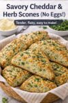 Basket of savory cheddar and herb scones with a fluffy interior, golden crust, and fresh herbs, styled with butter and green onions on a farmhouse table.